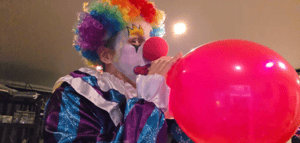 Quin69 in a clown outfit inflating a balloon